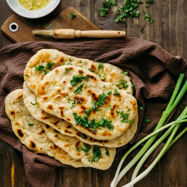 Freshly baked Indian naan bread, garnished with cilantro, on a brown cloth with green onions.