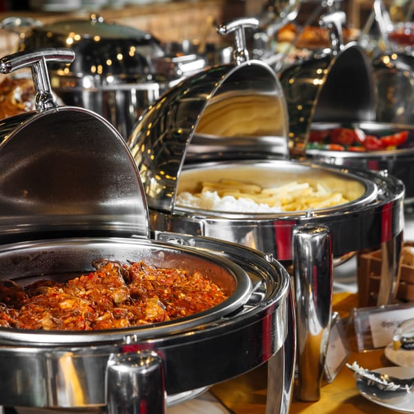 Indian buffet with chicken curry, rice, and french fries in shiny chafing dishes.
